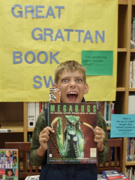 Boy making a wild face and holding a book titled Megabugs at a school literacy event