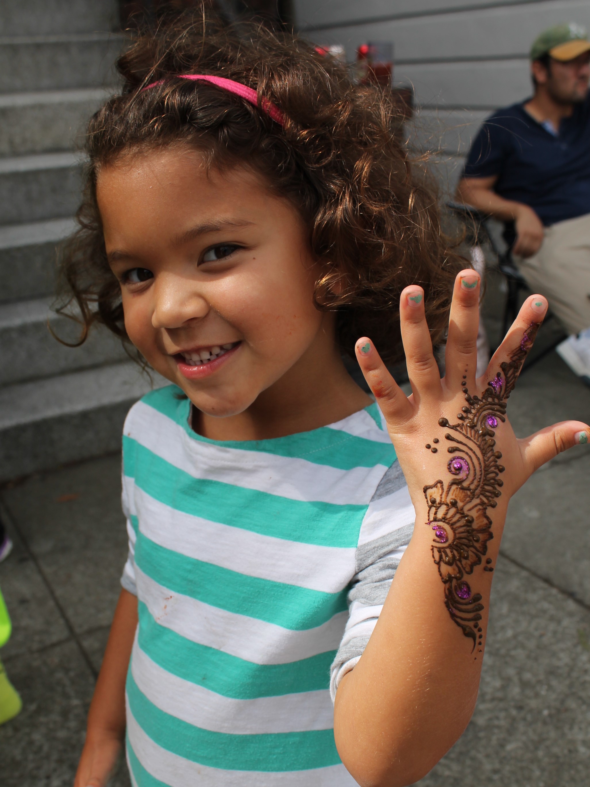Girl showing off the henna pattern on her hand at an outdoor neighborhood festival