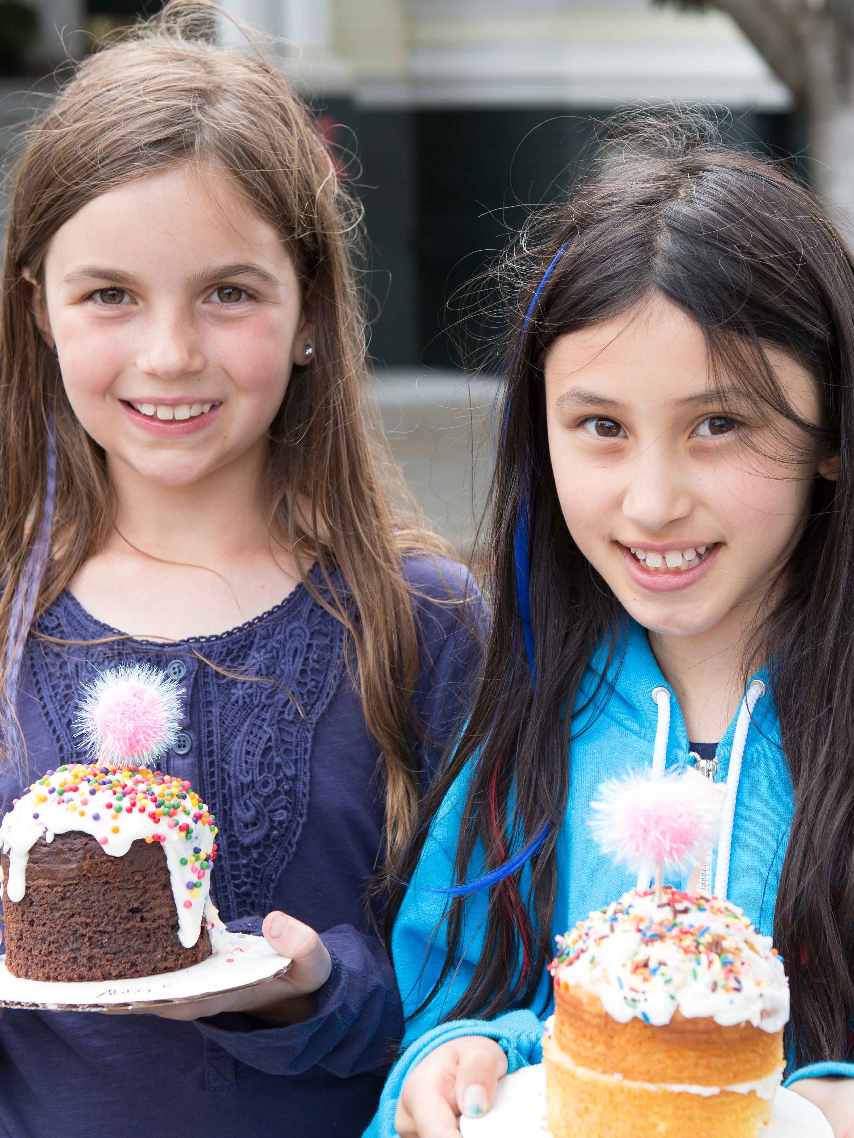 Two girls holding decorated cupcakes at an outdoor school festival