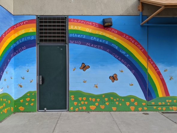 Colorful mural on exterior school wall, including painted rainbow with inspirational sayings