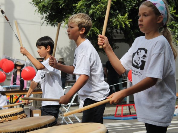 Children perform in a taiko drumming group at an outdoor neighborhood festival