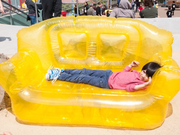 Boy lying in an inflatable yellow couch at an outdoor school festival