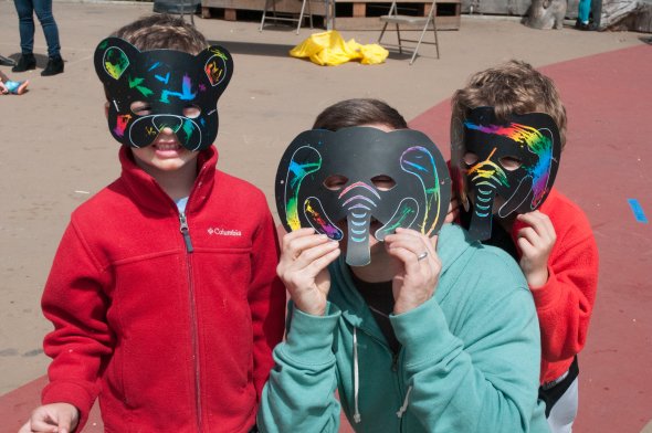 Two children and a parent wearing rainbow animal masks at a school festival