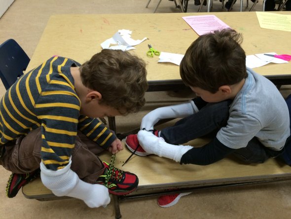 Boys with socks on their hands try to tie their shoes at a school inclusion awareness event