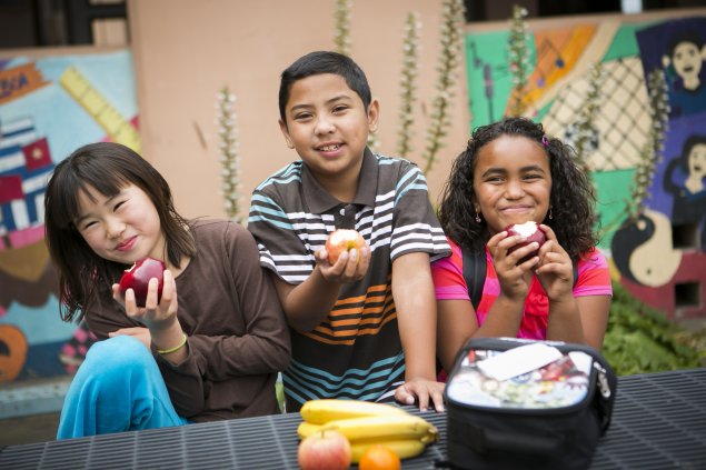 Three elementary school students eating apples